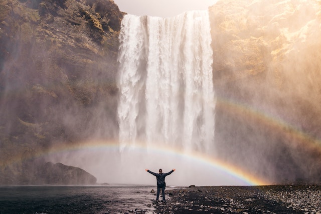 a man with his hands out in front of a waterfall and two rainbow 